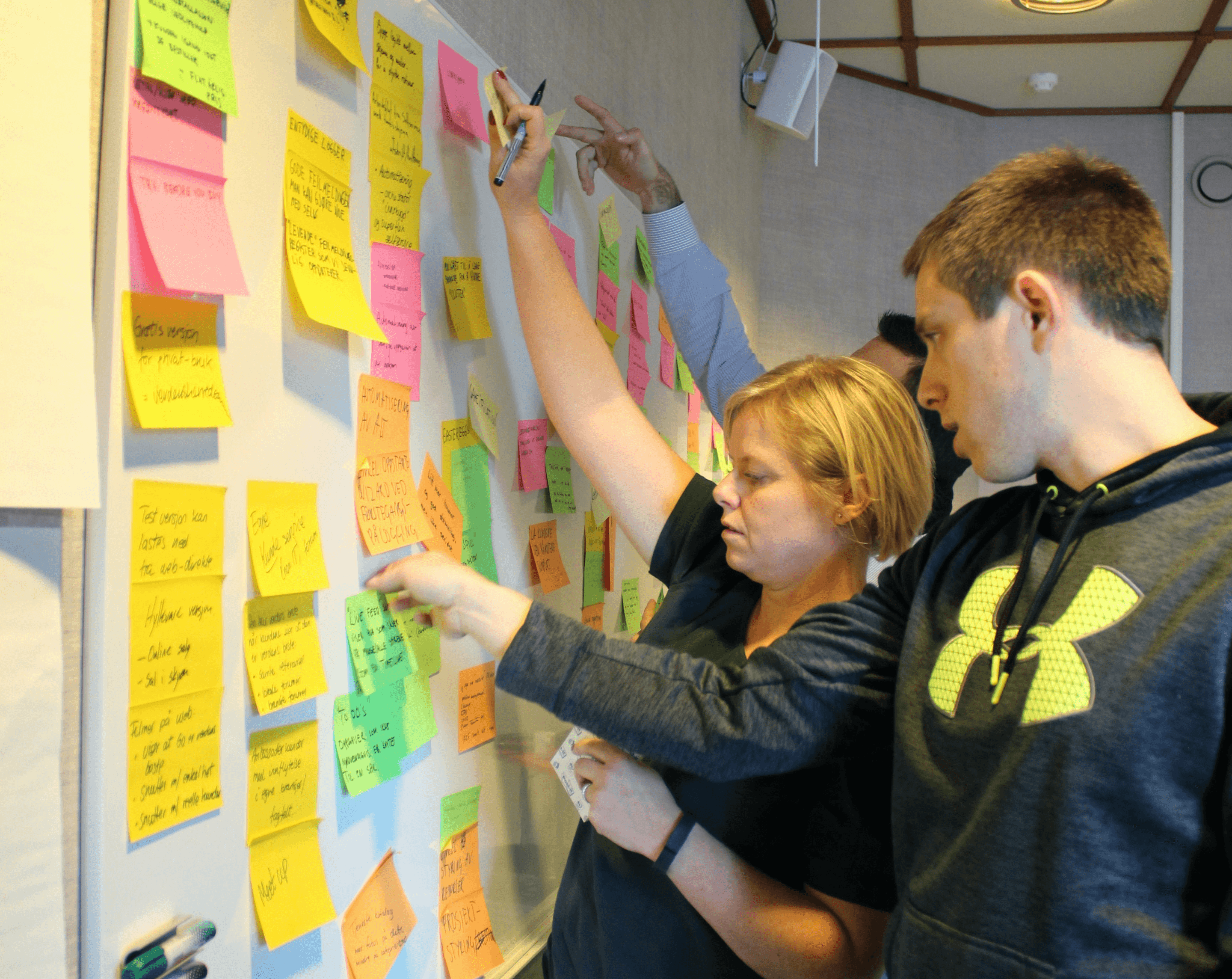 Three colleagues gathered around a whiteboard covered in colour-coded sticky notes during a workshop session.