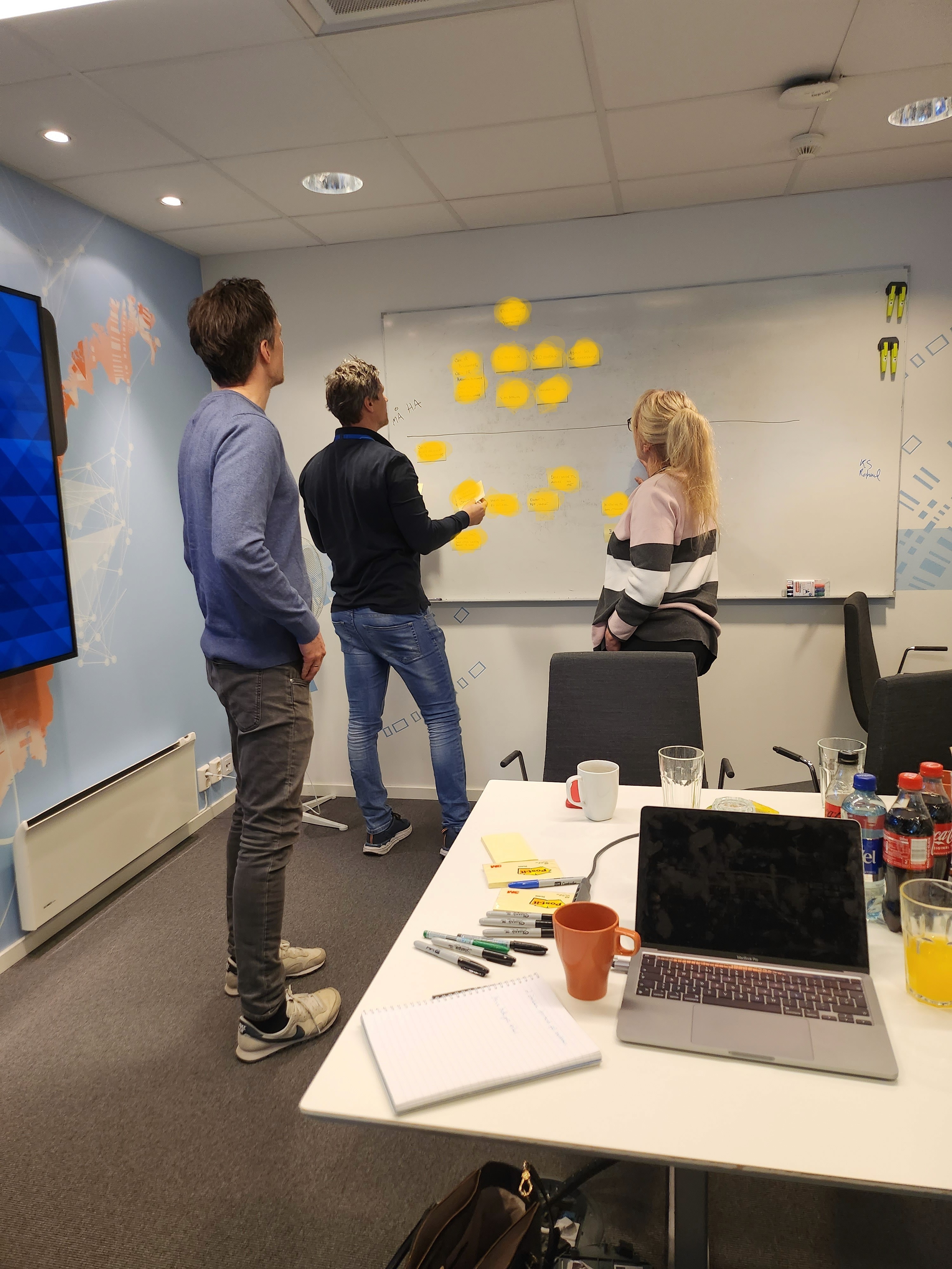 Three colleagues collaborating at a whiteboard covered in sticky notes during a workshop session.