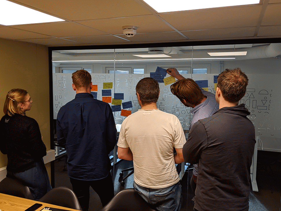 Five colleagues at a glass wall covered in sticky notes during an ideation workshop.