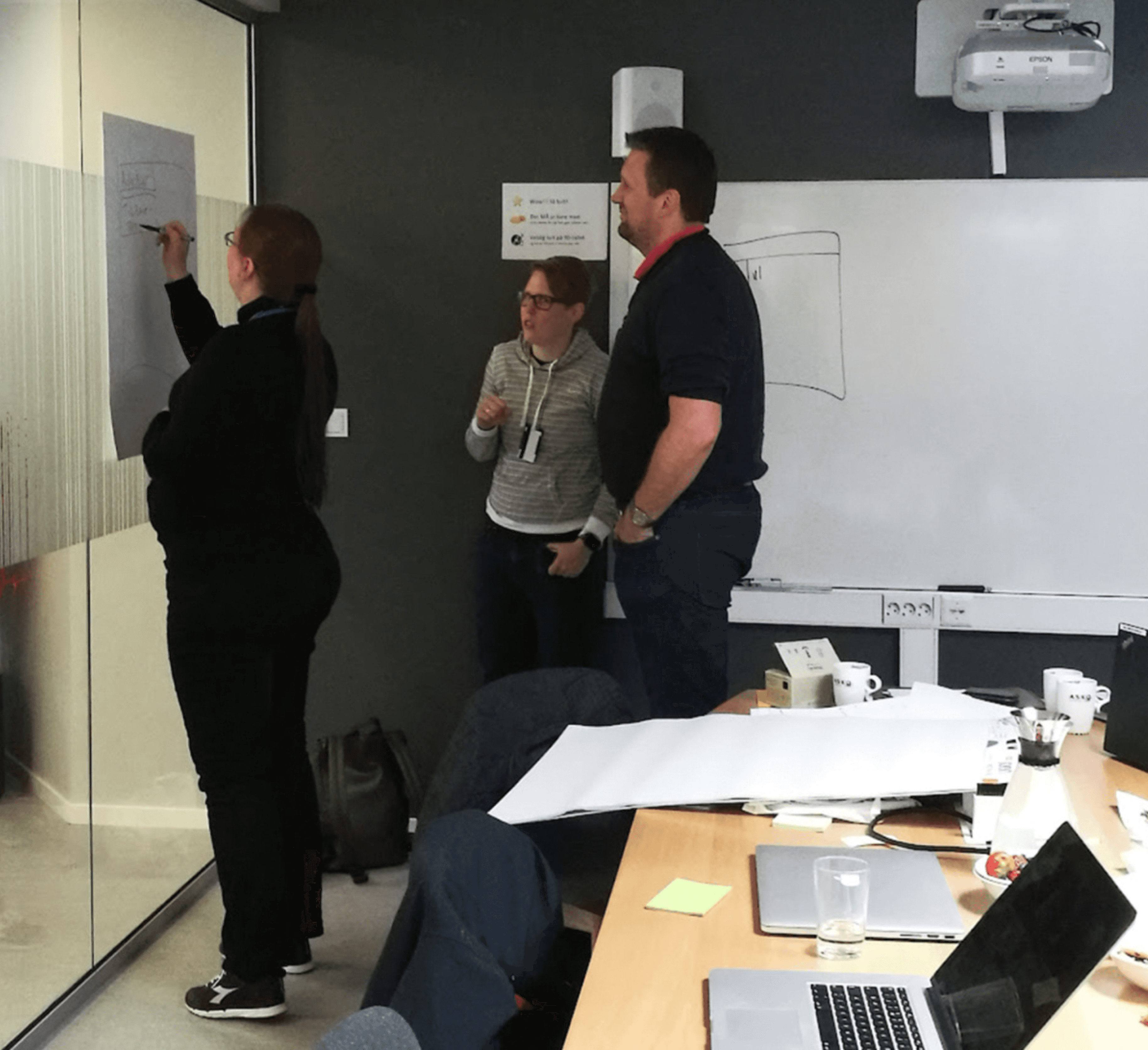 Three colleagues sketching an early concept on a whiteboard during a design workshop.